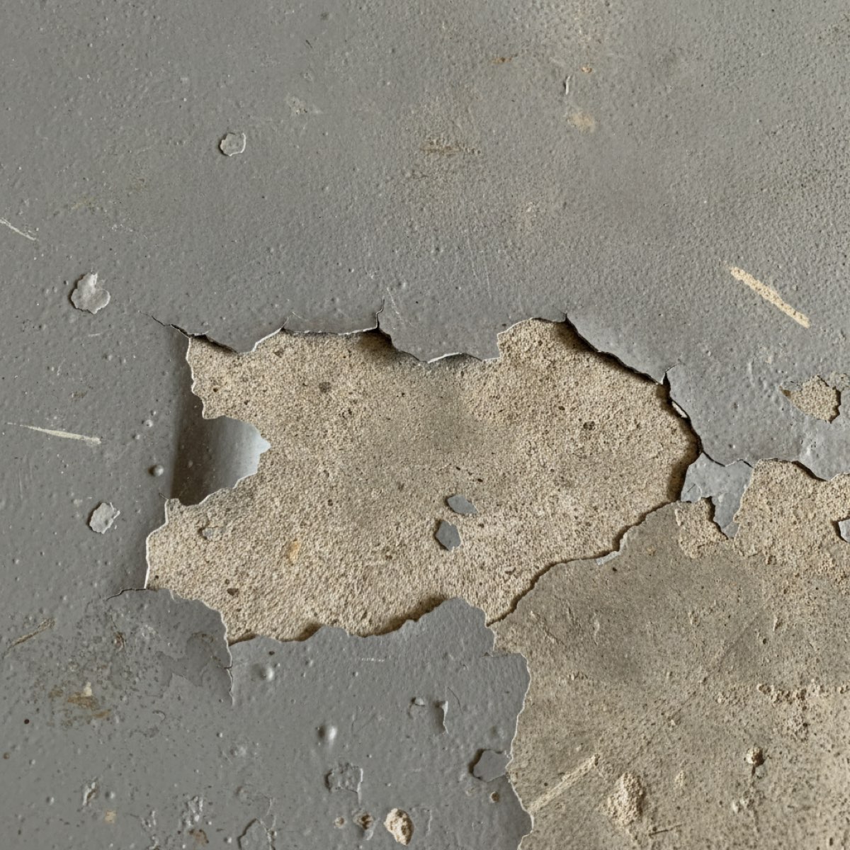 Close-up of garage floor paint peeling and flaking at the edge, showing bare concrete underneath